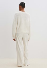 Flauschiger weißer Pullover mit langen Ärmeln und rundem Ausschnitt, kombiniert mit hellbeigen weit geschnittenen Hosen. Weiche Textur und lässige Passform.