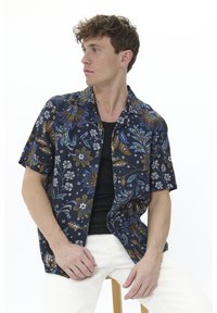 Cămașă cu mânecă scurtă, cu un model floral în culori închise, accentuată cu detalii albastre și aurii, având un design cu nasturi și o textură moale, purtată împreună cu un tricou negru.
