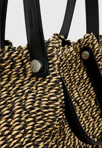 Borsa in paglia intrecciata nera e tonalità naturali, con manici in pelle nera liscia e bottoni metallici decorativi.