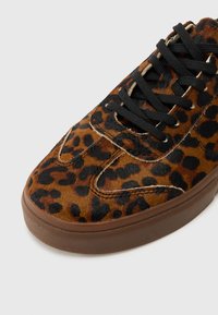 Snetters med leopardmønster som har en blatert tekstur, svarte snørebånd og en brun gummi såle. Overdelen er for det meste brun med svarte flekker.