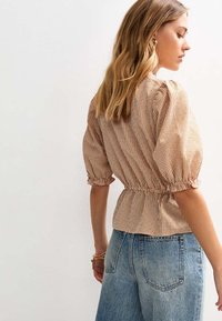 Brun rutig puffärmad topp med samlad midja, ihopparad med blå högmidjade jeans. Strukturerad tyg med elastiska ärmslut.
