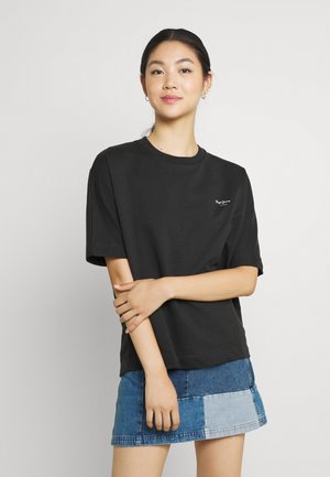 T-shirt in cotone nero con scollo rotondo e maniche corte, caratterizzato da un piccolo logo bianco sul petto, abbinato a una gonna in denim con applicazioni.