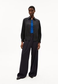 Black button-up shirt, blue fitted top, and wide navy striped trousers. Smooth fabric, long sleeves, and pointed black shoes.