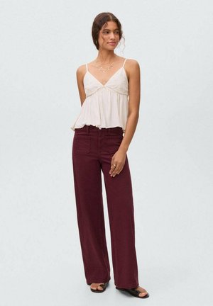 Witte, vloeiende cami-top met dunne bandjes en een gegatherde taille; gecombineerd met burgundy wijde broek met voortassen.