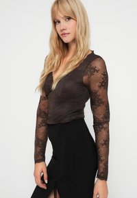Bruine kant lange mouwen top met een aansluitende bodice en diepe V-hals, gecombineerd met een zwarte rok met hoge taille en een zijsplit.