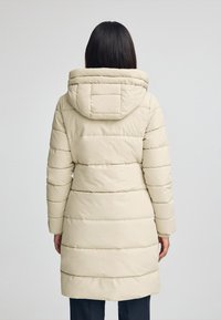 Abrigo acolchado beige con capucha, que presenta secciones acolchadas horizontales y puños elásticos. La parte posterior es sencilla con un diseño de capucha plana.