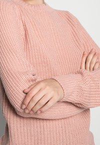 Różowy sweter dzianinowy o prążkowanej fakturze, okrągłym dekolcie i długich rękawach. Tkanina ma miękki wygląd i luźny, komfortowy krój.