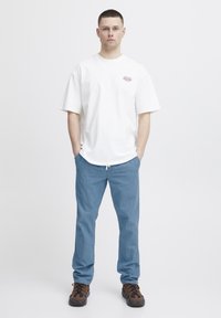 Camiseta de algodón blanca con mangas cortas, pantalones de algodón azul claro y zapatos de senderismo marrones con acentos negros. Atuendo simple y casual.