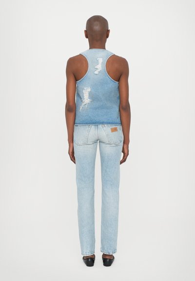 Denimist seljatop ja helesinised teksad. Topil on kulumiskohad; teksad on klassikalise lõikega ja nende taga on silt. Mustad kingad.