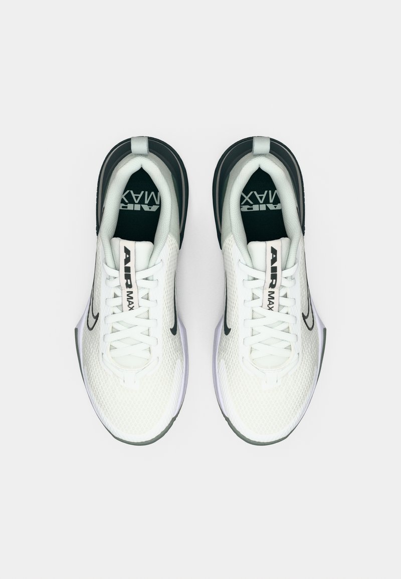 Zapatillas deportivas blancas con material de malla y acentos negros, con cordones, punta redondeada y una marca visible en la lengüeta.