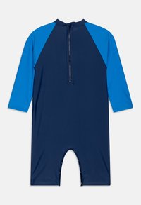Marineblå rash guard med lange ermer, kontrastfargede lyseblå skuldre, glidelås bak og trykknapper ved benåpningene.