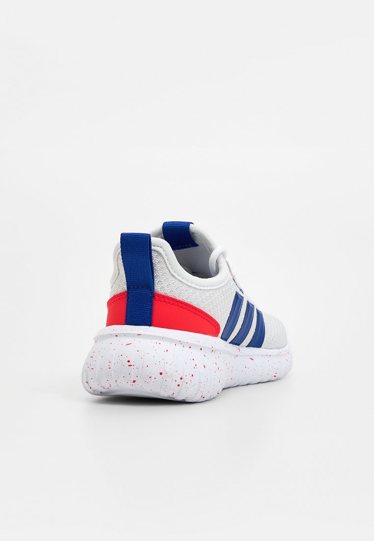Zapatilla deportiva blanca con detalles en azul y un talón rojo, con una parte superior texturizada, tres franjas azules y una suela blanca moteada.