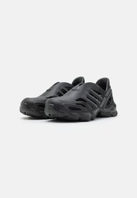 Crne slip-on cipele napravljene od fleksibilnog materijala, s izrezanim ventilacijama, teksturiranom površinom i konturiranim dizajnom đona.
