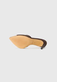 Une seule chaussure à talons hauts en daim marron vue par la semelle, avec un bout pointu et une semelle en caoutchouc texturé.