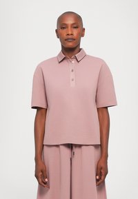 Kurzarm-Polohemd aus hellrosa Stoff mit umgeschlagenem Kragen, Drei-Knopfreihe und lässiger Passform. Glatte Textur und dezenter Glanz.