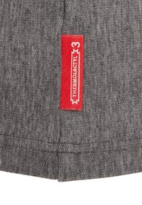 Grijs stof met een gestructureerd patroon, voorzien van een opvallend rood label met witte branding en het nummer 3 erop geborduurd.