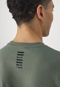 Felpa verde con collo rotondo e dettaglio a striscia nera verticale sul retro con larghezze variabili, realizzata in tessuto morbido.