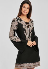 Vestido negro con intrincados patrones florales en rosa y blanco. Presenta un escote con lazo y mangas acampanadas. Adorno decorativo en el dobladillo.