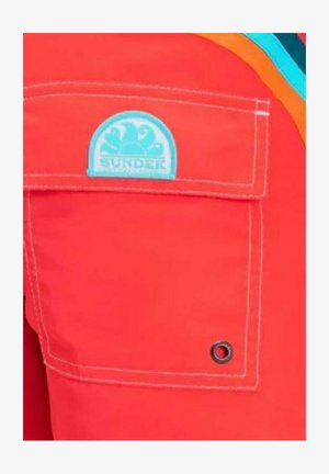 Tessuto rosso con una tasca che presenta un logo "SUNDEK" blu chiaro. Include cuciture bianche e un dettaglio in grommet nero sulla tasca.