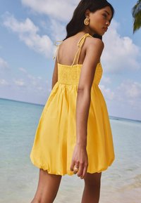 Geel zomerjurkje met smock-bustier, verstelbare bandjes en een uitlopende rok. Beschikt over een zachte textuur en een elastische tailleband voor comfort.