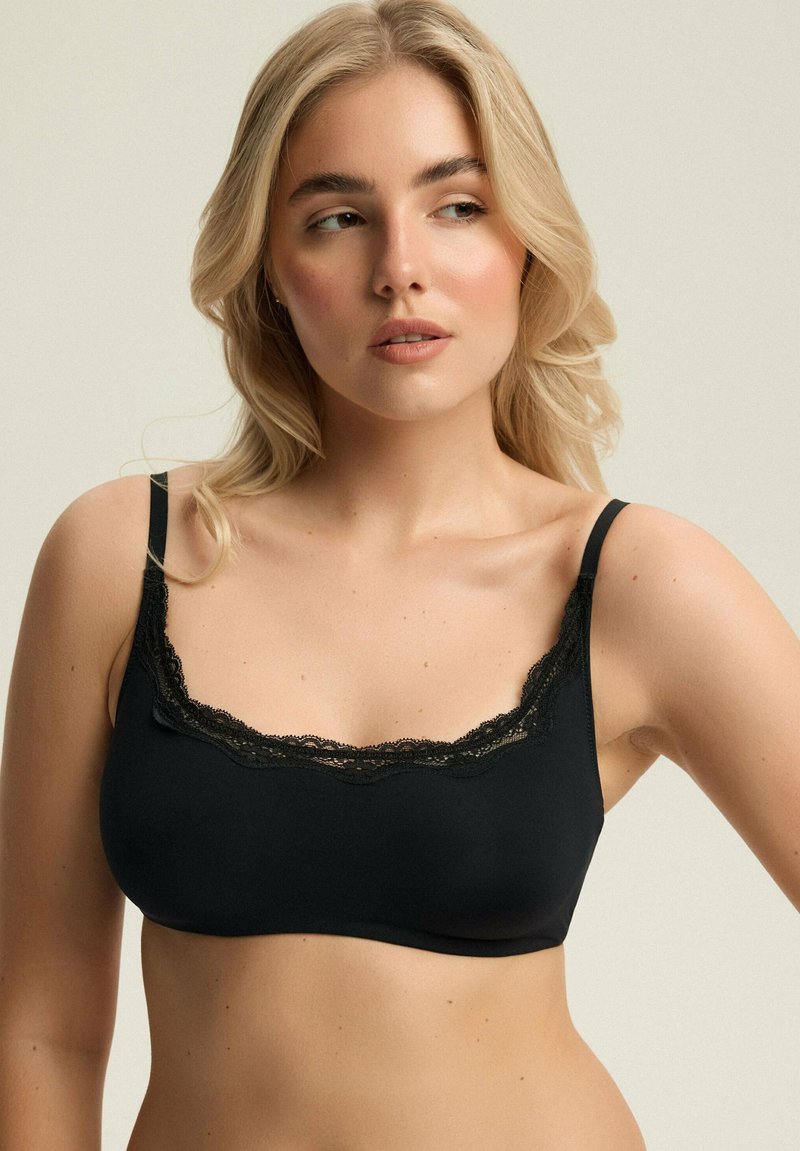 Czarny biustonosz braletka z koronkowym wykończeniem, z regulowanymi ramiączkami i bezszwowym designem, wykonany z miękkiej, elastycznej tkaniny dla komfortu.