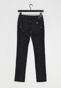 Jeans de mezclilla negra con un corte slim, diseño de cinco bolsillos, costuras visibles y una pequeña etiqueta de logo roja en el bolsillo trasero.