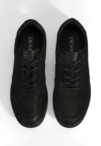 Baskets en cuir noir avec une texture lisse, bout rond, design à lacets et style minimaliste. Logo visible sur la semelle intérieure.