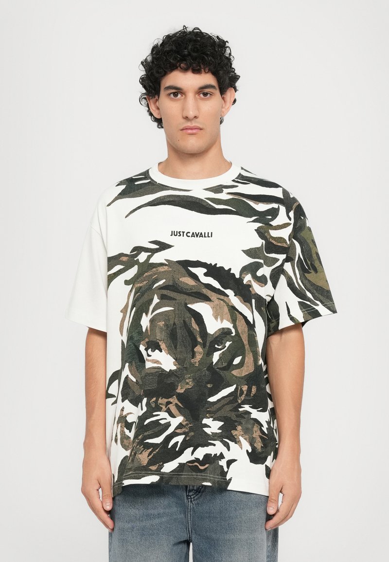 White cotton t-shirt featuring a large tiger graphic in green and brown tones, with "JUST CAVALLI" printed in black across the chest.