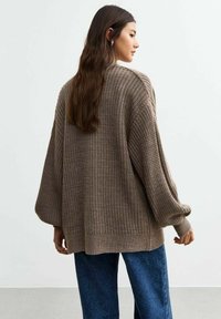 Cardigan oversize marrone a maglia con un motivo testurizzato, maniche larghe e una vestibilità rilassata, abbinato a pantaloni blu scuro.