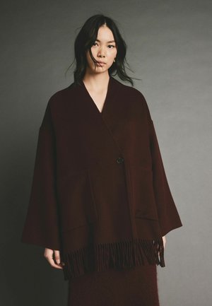 Burgundy színű, oversize kabát gyapjú keverékből, bojtolt aljjal, mély zsebekkel és egy gombos záródással.