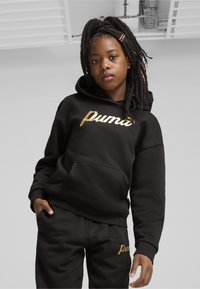 Felpa con cappuccio nera e pantaloni abbinati con logo "Puma" dorato. La felpa ha una tasca frontale; il tessuto appare morbido e spesso.