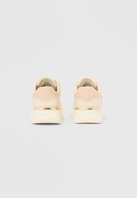 Krem roza športni copati z teksturirano površino, z zlatimi kovinskimi poudarki in debelim podplatom.