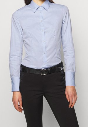 Lichtblauwe, colbert met een gladde stof, met een getailleerd ontwerp en knoopsluiting. Gekozen met zwarte broek en een gestructureerde riem.