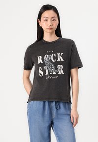 Črna bombažna majica s sproščenim krojem, ki ima obrabljeno besedilo "ROCK STAR" in svetlečo grafiko mačke. Kratki rokavi in okrogla izrez.