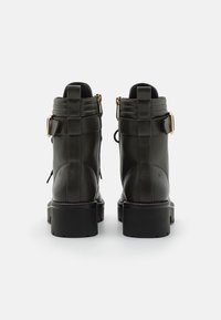 Botas de tobillo de cuero verde oscuro con una suela negra gruesa, que presentan una hebilla lateral y acentos texturizados en la parte superior.