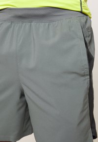 Graue Sportshorts aus leichtem, glattem Material. Mit einem elastischen Bund und seitlichen Taschen mit schwarzen Akzenten.