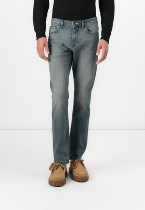 Jeans in denim blu sbiadito con taglio a gamba dritta. Presentano tasche frontali e chiusura con zip. Indossati con scarpe in suede marrone chiaro.