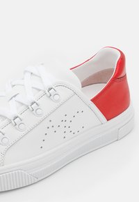 Baskets en cuir blanc avec talon rouge, lacets ton sur ton, détails perforés et semelle en caoutchouc blanc texturé avec des stries subtiles.