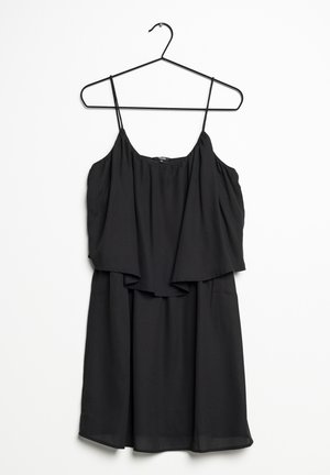 Robe noire sans manches avec fines bretelles suspendue sur un cintre noir sur un fond blanc.