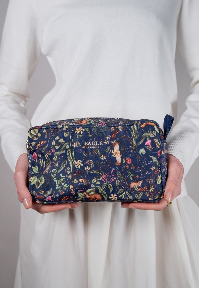 Pochette cosmetica floreale in tessuto blu navy con una varietà di illustrazioni botaniche colorate. Chiusura con zip e manico laterale attaccato.