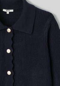 Cardigan en maille côtelée bleu marine avec une patte de boutonnage festonnée et des boutons métalliques. Présente un col classique. Taille S.