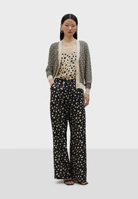 Pletena kardigan jakna s ribanim uzorkom, bež dugmad, uparen s bež majicom s točkicama i crnim širokim hlačama s velikim krem točkama.