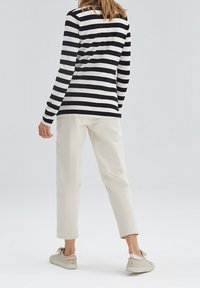 Gestreiftes Langarmhemd in Marineblau und Weiß, lässige cremefarbene Hose und helle Sneakers, von hinten vor einem schlichten Hintergrund betrachtet.