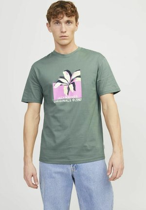 Grøn bomulds T-shirt med grafisk tryk af blade på en lyserød baggrund. Korte ærmer, rund halsudskæring og afslappet pasform. Let tekstur.