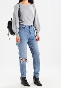 Gray long-sleeve shirt with textured puff sleeves, blue distressed high-waisted jeans, and black ankle boots. Black backpack.