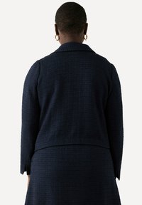 Giacca textured blu navy con un design strutturato, colletto a vista e maniche lunghe. Il tessuto presenta un motivo sottile e una vestibilità su misura.