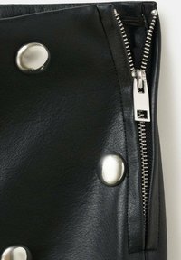 Prenda de cuero negro con un zipper plateado y botones de metal. La textura es suave, con un ligero brillo; el diseño es elegante y moderno.