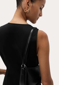 Sac à bandoulière en cuir noir au toucher lisse et au design épuré, avec une fine sangle et une fermeture éclair discrète.