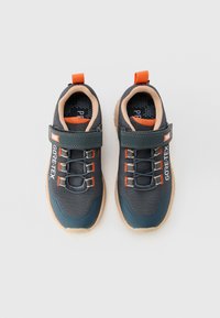 Un paio di scarpe sportive Gore-Tex grigio scuro e arancioni con lacci elasticizzati e cinturini in Velcro su uno sfondo bianco.