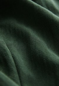 Gros plan d'un tissu côtelé vert foncé montrant des lignes verticales texturées, tissées serrées et des plis doux.